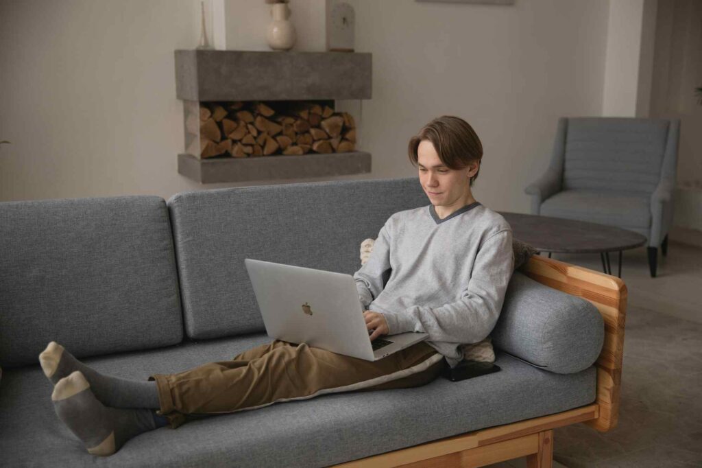 A remote developer is working from home, sitting on a couch with a laptop in front of them. They appear focused and comfortable, with a cozy atmosphere in the room.
